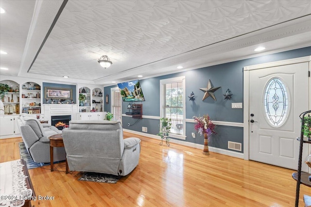 living room with a textured ceiling, light hardwood / wood-style floors, built in features, and crown molding