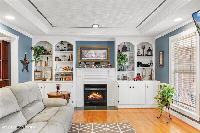 living room featuring a raised ceiling, built in shelves, crown molding, and light hardwood / wood-style flooring