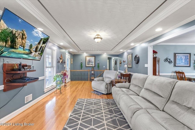 living room featuring wood-type flooring, a textured ceiling, a raised ceiling, and ornamental molding