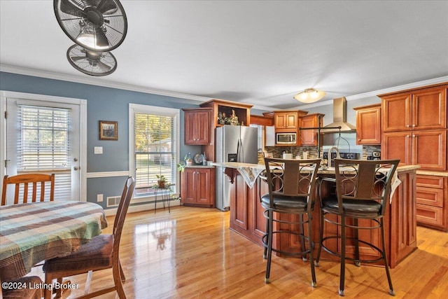 kitchen featuring appliances with stainless steel finishes, light wood-type flooring, crown molding, and wall chimney range hood