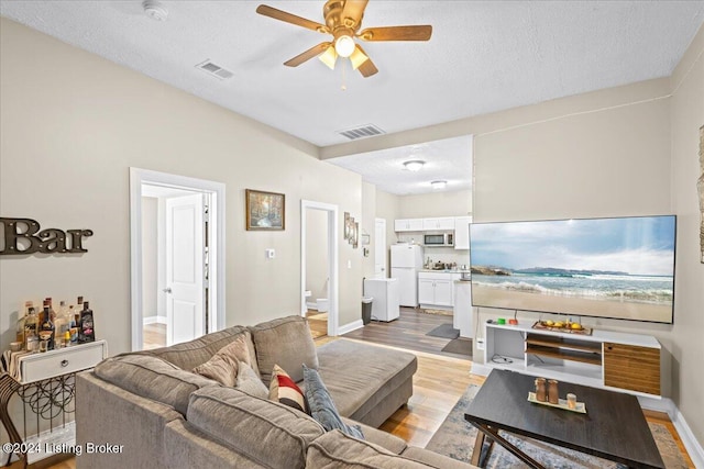 living room featuring a textured ceiling, light hardwood / wood-style flooring, and ceiling fan