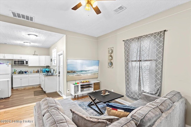 living room with ceiling fan, a textured ceiling, and light wood-type flooring