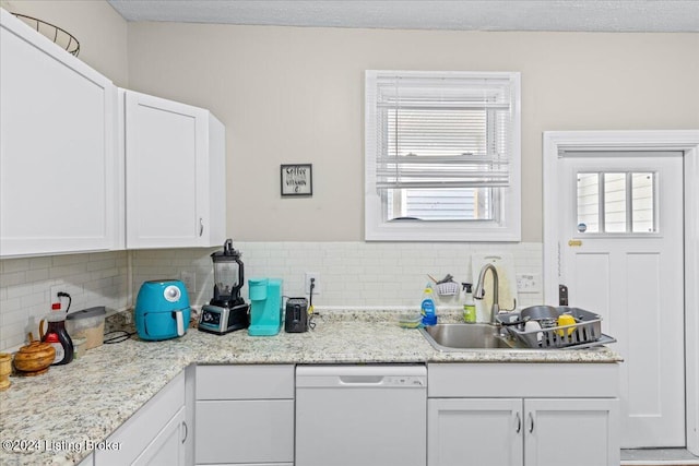 kitchen featuring white cabinetry, dishwasher, sink, light stone counters, and backsplash