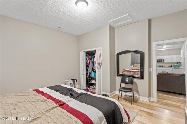 bedroom with a textured ceiling, a spacious closet, light hardwood / wood-style flooring, and a closet