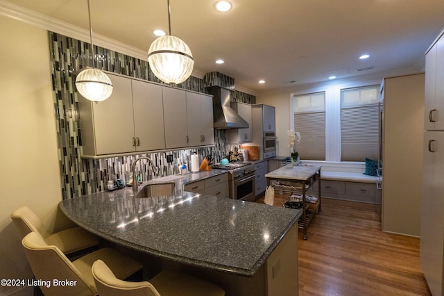 kitchen with pendant lighting, dark stone counters, sink, wall chimney exhaust hood, and decorative backsplash