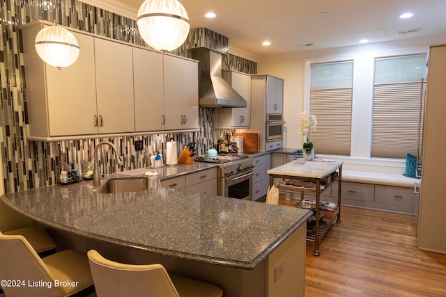 kitchen featuring wall chimney range hood, sink, light wood-type flooring, ornamental molding, and appliances with stainless steel finishes