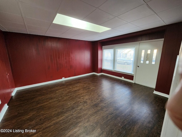 unfurnished room featuring wood walls, a drop ceiling, and dark hardwood / wood-style floors