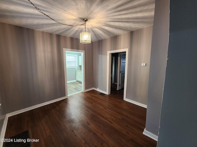 unfurnished room with a chandelier and dark wood-type flooring