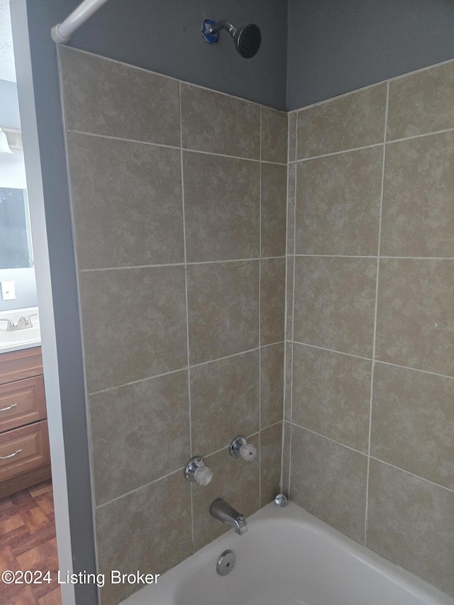 bathroom with tiled shower / bath combo, parquet flooring, and vanity