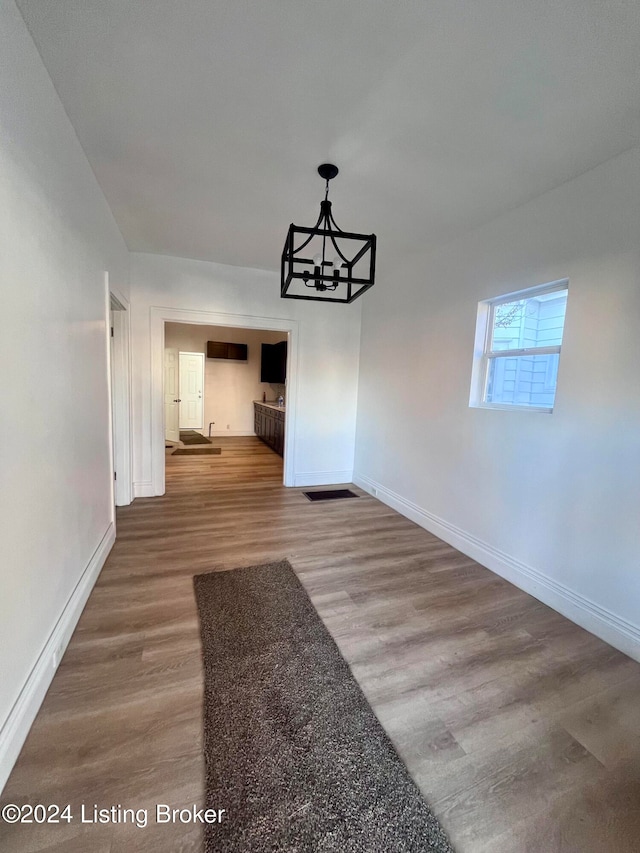 unfurnished dining area with wood-type flooring and a notable chandelier