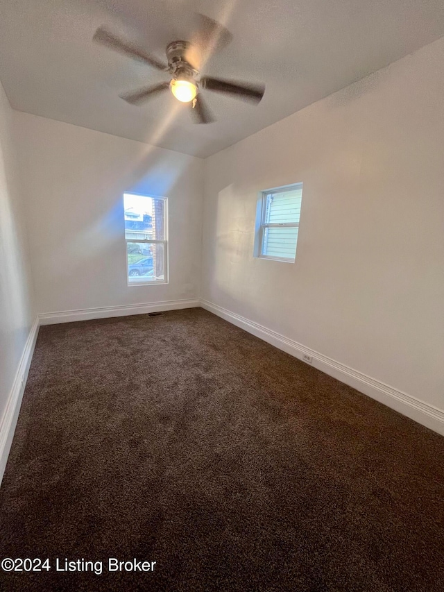 spare room featuring dark colored carpet and ceiling fan