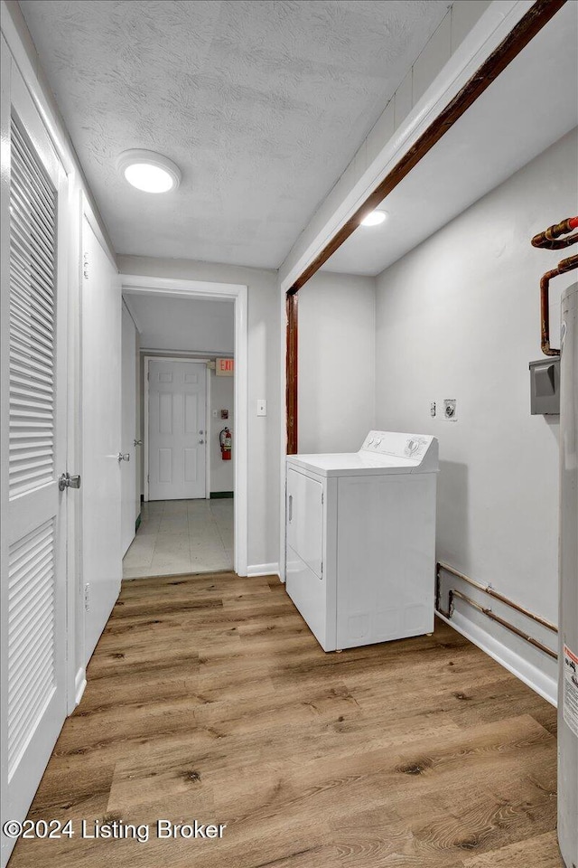 clothes washing area with washer / dryer, a textured ceiling, and light hardwood / wood-style floors