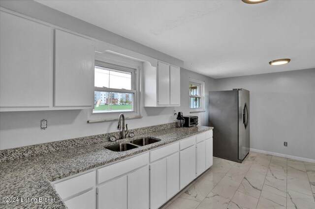 kitchen with white cabinets, light stone countertops, sink, and stainless steel refrigerator