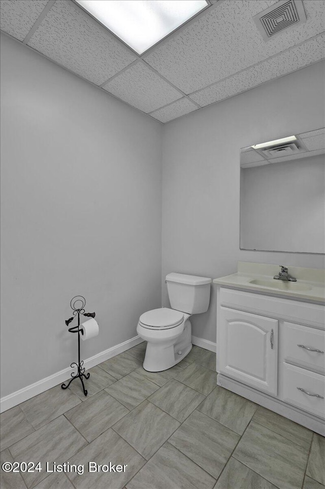 bathroom with a paneled ceiling, vanity, toilet, and tile patterned floors