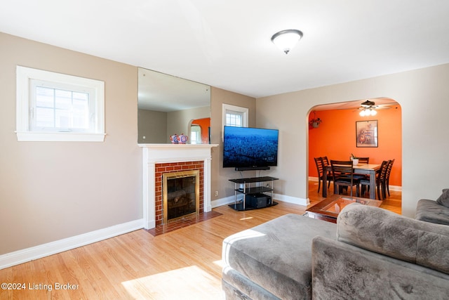 living room featuring ceiling fan, wood-type flooring, and a brick fireplace