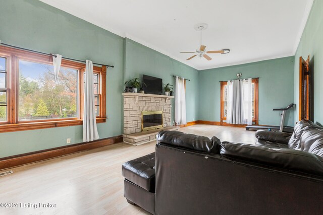 living room with a stone fireplace, ceiling fan, and light wood-type flooring