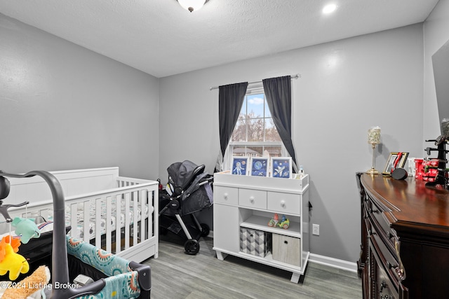 bedroom featuring hardwood / wood-style flooring, a crib, and a textured ceiling