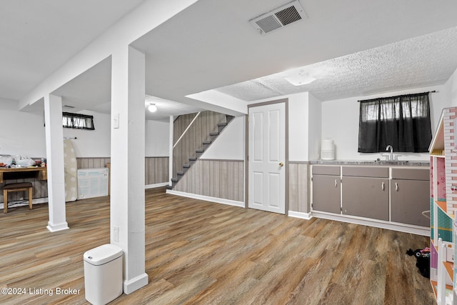 basement featuring sink, light wood-type flooring, a textured ceiling, and wooden walls