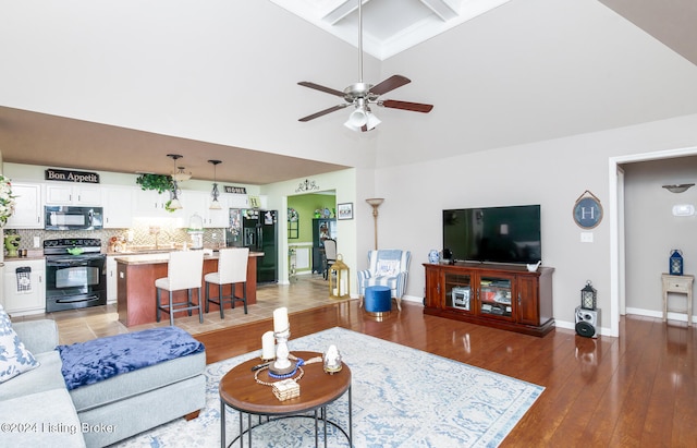 living room featuring a towering ceiling, ceiling fan, sink, beam ceiling, and hardwood / wood-style floors