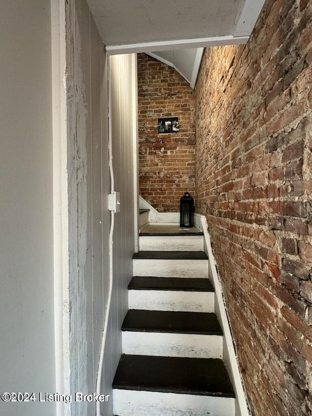 stairway featuring brick wall and vaulted ceiling