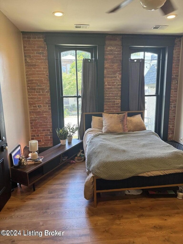 bedroom with ceiling fan, wood-type flooring, and brick wall