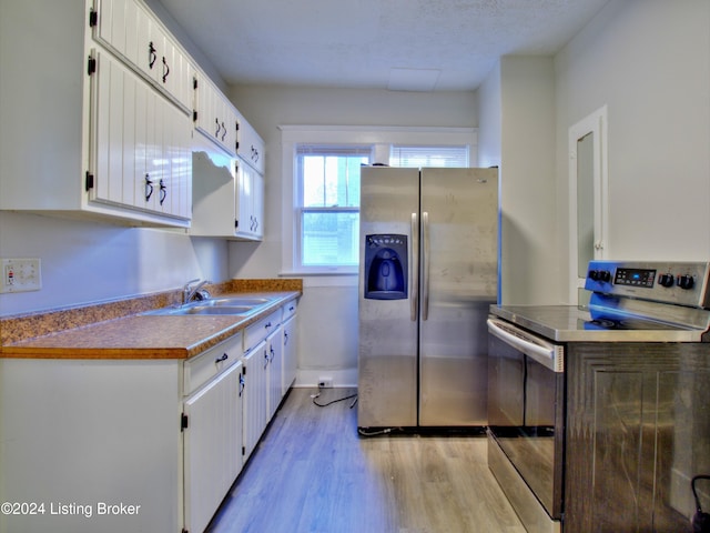 kitchen featuring light wood-type flooring, a textured ceiling, stainless steel appliances, sink, and white cabinets