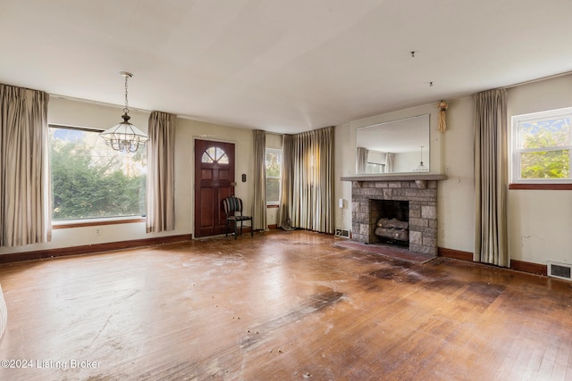 unfurnished living room with a chandelier, hardwood / wood-style floors, and a stone fireplace