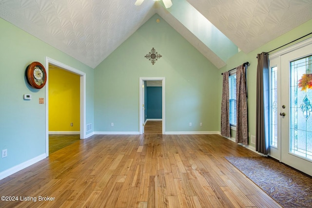 unfurnished living room featuring vaulted ceiling with skylight, ceiling fan, light wood-type flooring, and a wealth of natural light