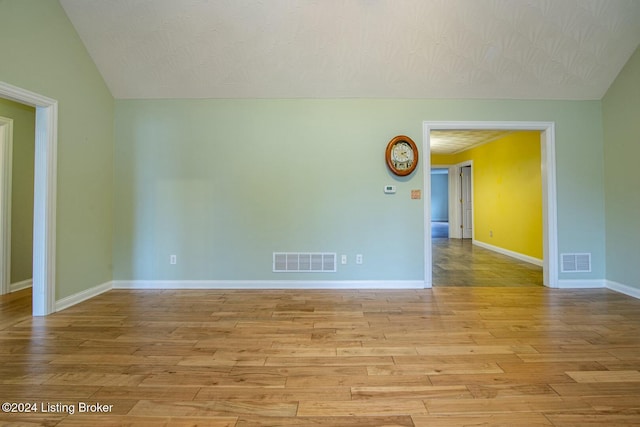 spare room featuring a textured ceiling, light hardwood / wood-style flooring, and lofted ceiling