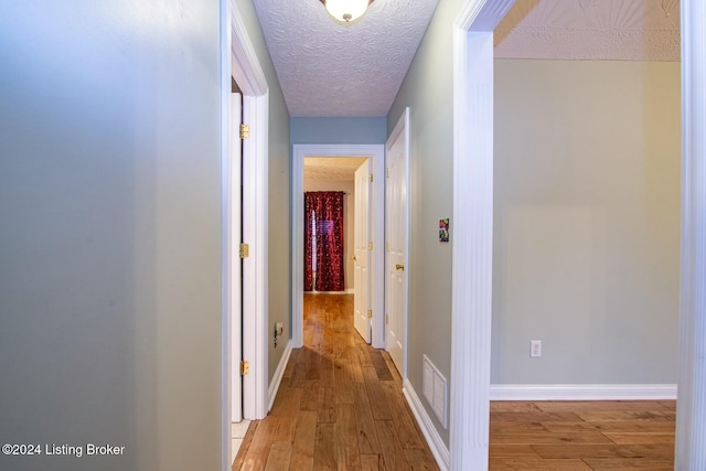 hallway with light hardwood / wood-style floors and a textured ceiling