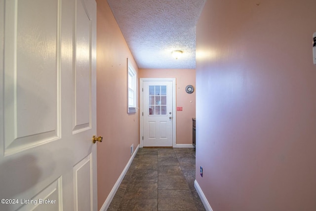 doorway to outside featuring dark tile patterned floors and a textured ceiling