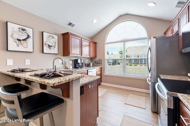 kitchen featuring light stone counters, a breakfast bar, stainless steel appliances, vaulted ceiling, and light hardwood / wood-style flooring