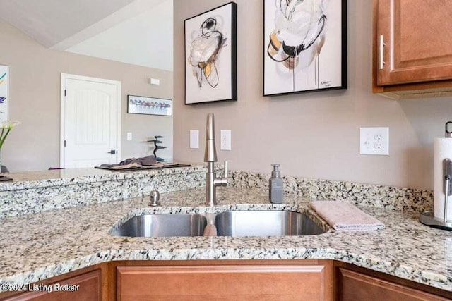 kitchen with lofted ceiling, light stone countertops, and sink