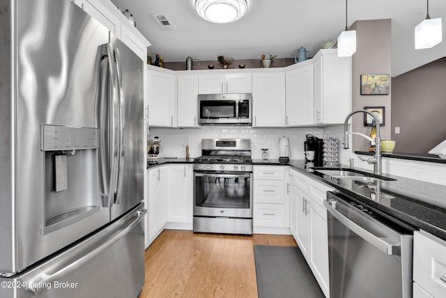 kitchen featuring appliances with stainless steel finishes, backsplash, dark stone counters, decorative light fixtures, and light hardwood / wood-style floors