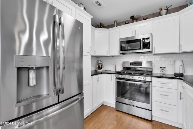 kitchen with white cabinets, backsplash, stainless steel appliances, and light hardwood / wood-style flooring