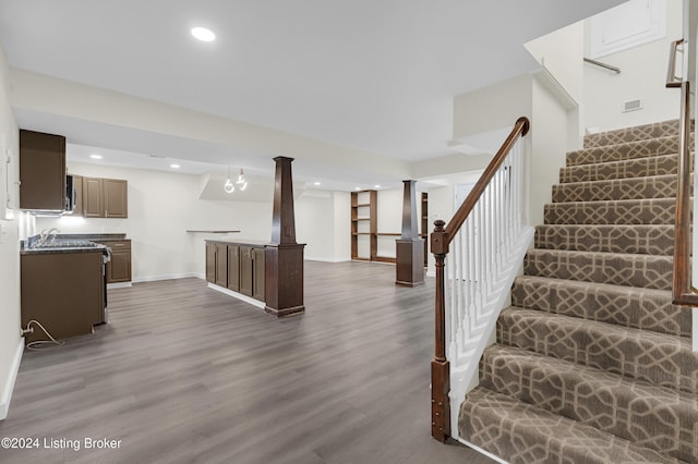 stairway featuring an inviting chandelier, wood-type flooring, sink, and decorative columns