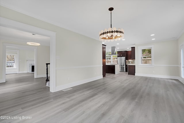 unfurnished living room featuring light wood-type flooring, ornamental molding, and an inviting chandelier