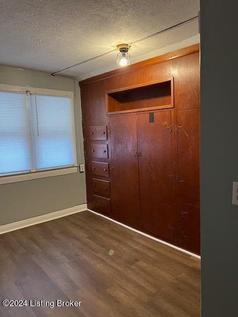 unfurnished bedroom with a textured ceiling, dark wood-type flooring, and a closet