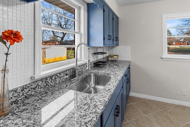 kitchen with light stone countertops, blue cabinets, sink, and light tile patterned floors