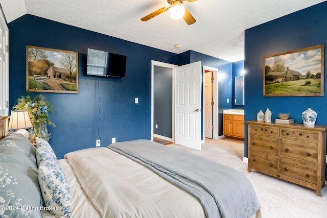 bedroom with ensuite bathroom, a textured ceiling, light colored carpet, vaulted ceiling, and ceiling fan