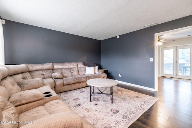 living room with a textured ceiling, ceiling fan, and dark wood-type flooring