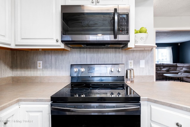 kitchen with a textured ceiling, white cabinetry, and black range with electric stovetop