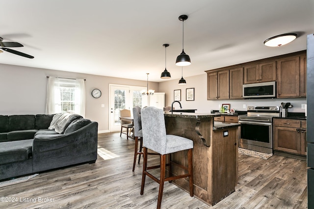 kitchen with hanging light fixtures, a kitchen breakfast bar, dark hardwood / wood-style flooring, a center island with sink, and appliances with stainless steel finishes