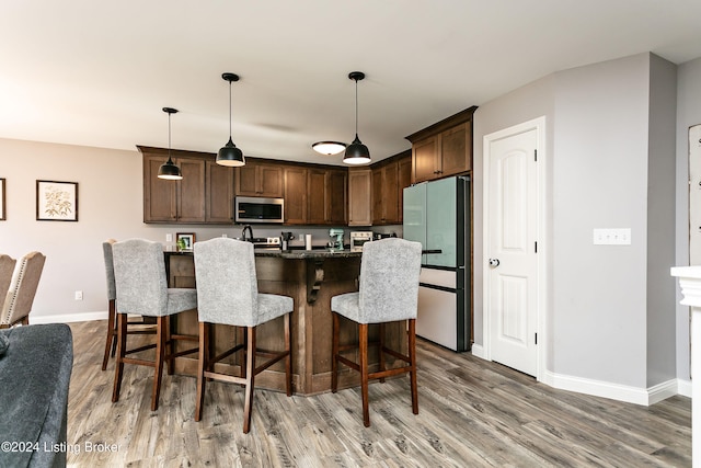 kitchen featuring hardwood / wood-style floors, hanging light fixtures, appliances with stainless steel finishes, dark brown cabinets, and a breakfast bar area