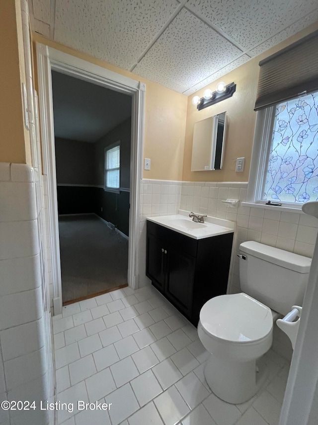 bathroom featuring a paneled ceiling, vanity, tile walls, tile patterned flooring, and toilet