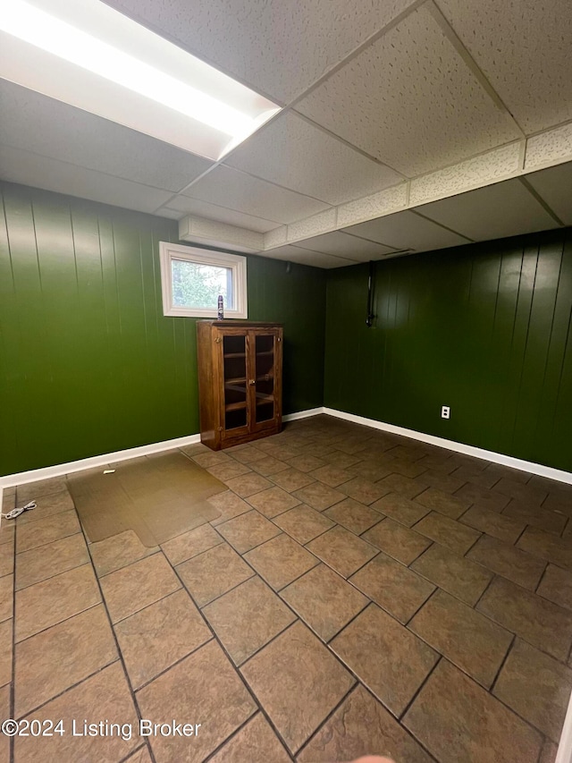 basement featuring a paneled ceiling, wooden walls, and tile patterned flooring