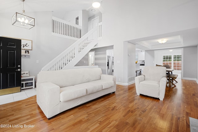 living room with high vaulted ceiling, light hardwood / wood-style floors, an inviting chandelier, and a tray ceiling