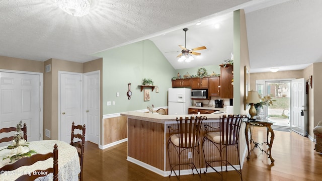 kitchen featuring kitchen peninsula, a textured ceiling, dark wood-type flooring, white fridge with ice dispenser, and lofted ceiling