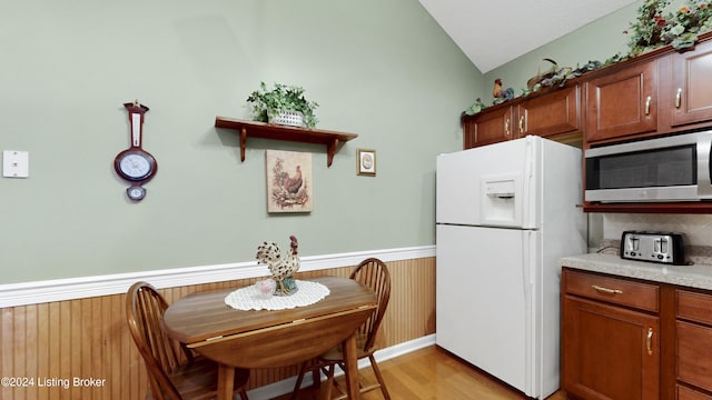 kitchen featuring light hardwood / wood-style flooring, wooden walls, white refrigerator with ice dispenser, vaulted ceiling, and decorative backsplash