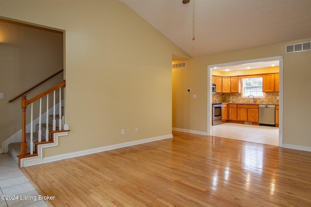 unfurnished living room with sink, vaulted ceiling, and light wood-type flooring